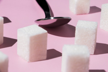 square pieces of cane sugar and a metal spoon on a pink background