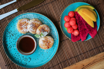 Vegan tofu cheese pancakes on blue plate with fresh tropical fruits and coconut cream, top view