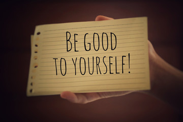 Inspirational quote - Be good to yourself. With a paper note in young woman hand on light brown...