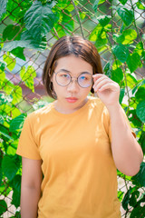 Happy Asia woman wearing glasses is looking into the camera for a portrait on the street on a background of green bushes
