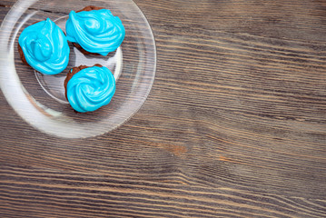 three handmade cupcakes with blue cream in a plate on a wooden table, top view
