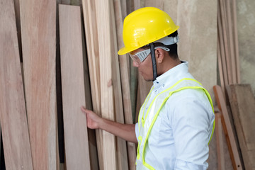 Handsome man wearing safety vest and put yellow helmet on head,choosing timber board,doing wood work at factory,Handmade design