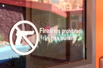 Fototapeta na wymiar Firearms prohibited sign on the glass entrance door to establishment notifies patrons that weapons aren't allowed, and addresses security policy and protection concerns