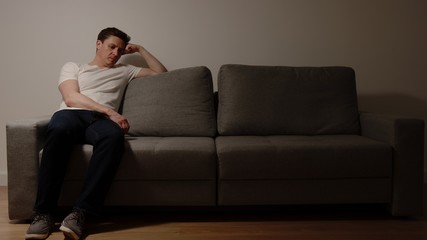Depressed young adult man on a grey sofa in the night