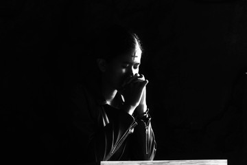 Ash Wednesday concept with young woman kneel in prayer pose in the church in black dark and white...