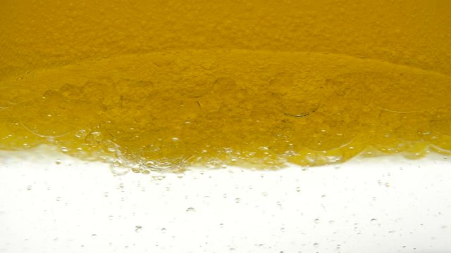 Sunflower oil is poured into a glass container. Close-up view of bio fuel shot in a research laboratory. A golden background of poured sesame oil and black cumin oil, resulting in bubbles and bulbs.