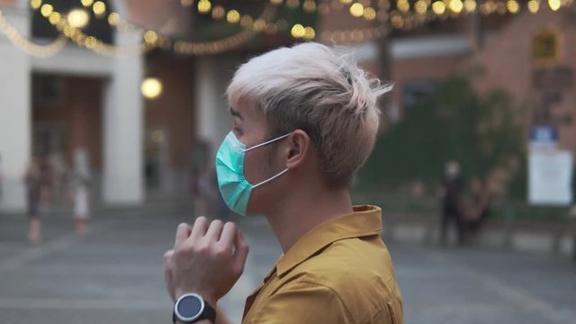 4K side portrait of young Asian man wearing a hygienic mask in public area.