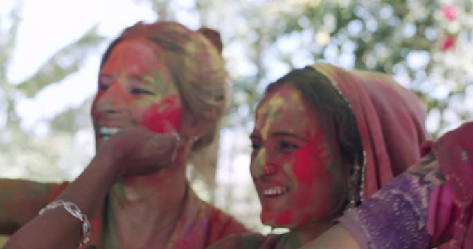 Western European Latin tourist couple enjoying joy playing kissing flirting coloring with local Rajasthani women in traditional clothes dress during the colour festival of Holi in India, handheld CU 