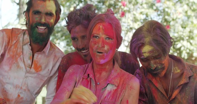 Close-up of female caucasian tourist celebrating festival of colours Holi in India with Indian men, put colors pose photo video selfie on vacation friendship, slow-motion handheld 60fps CU panning