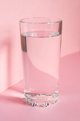Close up of sparkling water in transparent high glass and sun glare on pink background