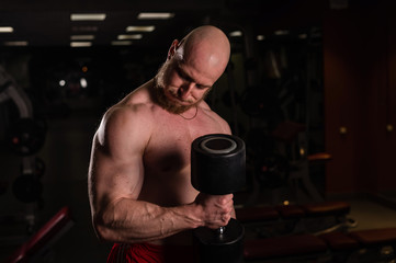 Shirtless handsome man doing biceps and triceps exercises with dumbbell. Embossed bodybuilder with...