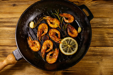 Grilled shrimp with spices, rosemary and lemon in a grill frying pan on a wooden table. Top view