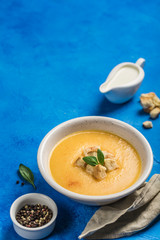 Pumpkin and carrot soup with cream and spinach with crackers on a classic blue background.