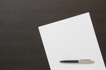 Template of white paper with pen on dark wenge color wooden background.