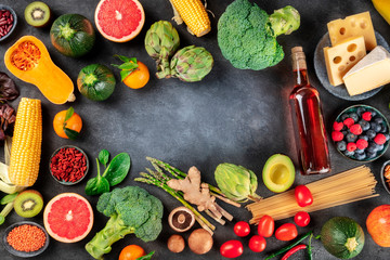 Food and wine, overhead shot of fruits, vegetables, cheese, pasta, legumes, mushrooms, and a bottle of wine, forming a frame on a dark background with a place for text