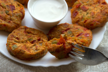 Vegetarian fried vegetable cutlets made of pepper, zucchini, potatoes, carrots and beans. Dish on a white plate with sour cream.