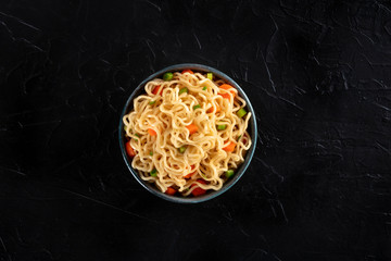 Instant noodles with carrot and scallions, vegetable soba in a bowl, shot from the top on a black...