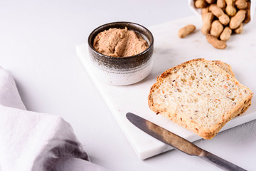 Homemade peanut paste or butter in a bowl and bread and peanuts on white marble tray. Healthy nutrition. Selective focus