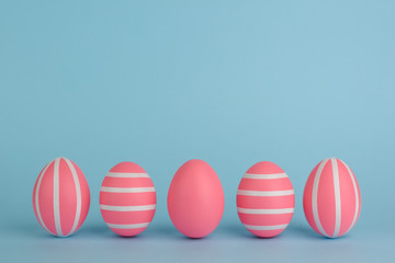 Easter decorated pink eggs. Five striped pink eggs in a row on a blue background. Isolated. White stripes. Colourful Easter concept. Copy space. Happy Easter card.