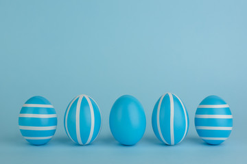 Easter decorated blue eggs. Five striped blue eggs in a row on a blue background. White stripes stripes. Monochrome concept. Copy space. Happy Easter card.