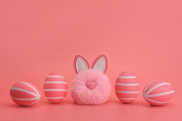 Funny easter pink rabbit pompom between pink striped eggs. White stripes on pink eggs. Pink background. Monochrome Easter concept. Easter card, design, banner. Copy space, place for text.