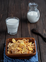 Jug and glass of milk , corn cereals in a wooden plate on dark wooden table. Close up. Shallow depth of field.