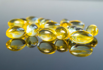 Fish oil capsules isolated on grey background with reflections, healthy Vitamin supplementation concept,close up shot. Shallow depth of field.