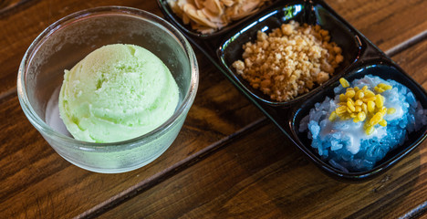 Delicious fresh homemade avocado ice cream scoop in bowl with three toppings in black ceramic container on wooden table in icecream shop