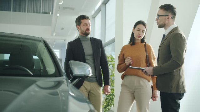 Young family husband and wife are purchasing automobile in car dealership talking to sales manager discussing deal. Communication and business concept.