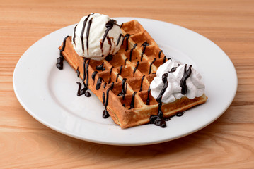 Plate of belgian waffles dessert with ice cream and chocolate caramel sauce on wooden table background.