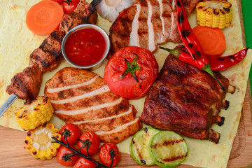 Top view of grilled meal of steak and vegetables spread out on rustic wooden board over bright green background