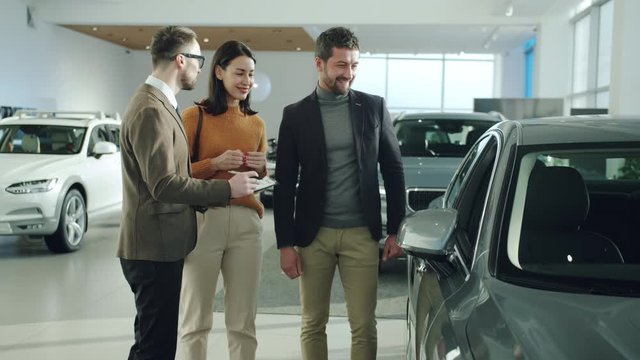 Friendly and professional car dealer is discussing new auto with cheerful clients man and woman concentrated on making deal. Business and transport concept.