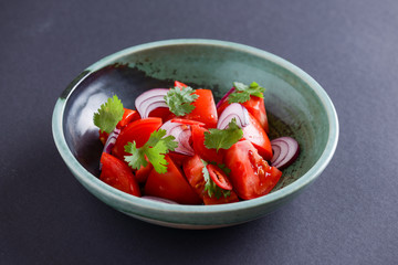 Healthy vegan lunch bowl. Ukrainian cuisine. Tomatoes with raw onions and parsley in a bowl on wooden table.