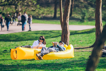 couple laying on yellow inflatable mattress in city park. reading book. drinking smoothies