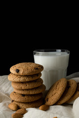 Oat cookies with chocolate, almond, milk in a transparent glass on white cloth over black background