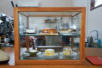 A wooden display case box filled with choux cream ,lemon butter cake ,mango short cake ,matcha...