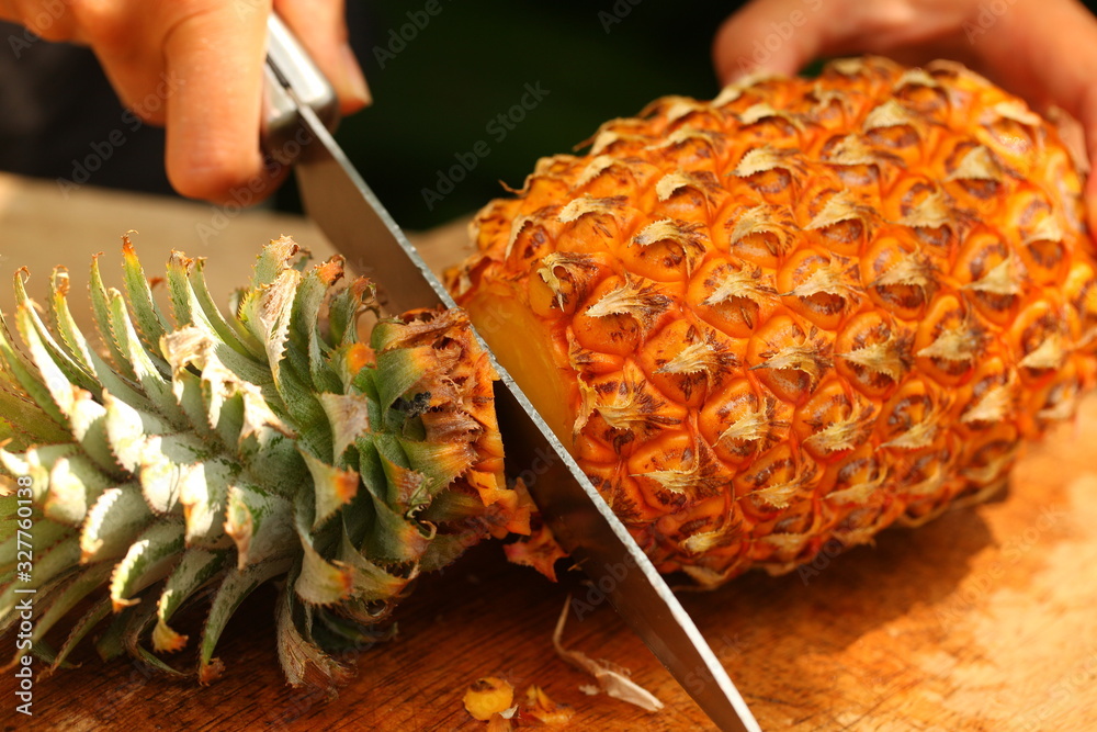 Wall mural fresh ripe pineapple slicing girl hands on a wooden table in a tropical garden