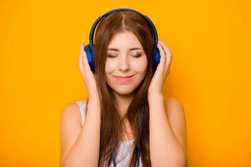 Close Up portrait of a beautiful, young woman listening to music with headphones, standing on a yellow background.