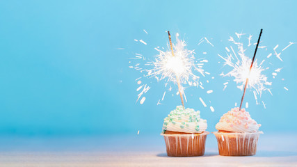 Two cupcakes decorated with colorful sprinkles and sparklers. Festive cupcakes on blue background...