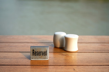 A used "Reserved" metal sign is on wood table.  White ceramic containers are in blurred background.