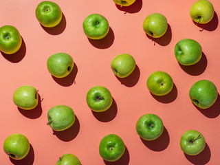 Green apples on orange or coral pink background pattern. Colorful fruit frame. Flat lay or top view, Hard light. Creative concept.