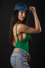 Fashion photo of beautiful brunette caucasian woman with long hair, sexy woman wearing green swimsuit jeans and cap.