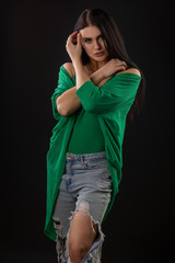 Portrait of a beautiful, young woman in a green top and jeans on a black background