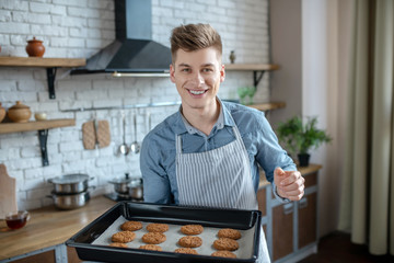 Young man with baking sheet of home baking in hands.
