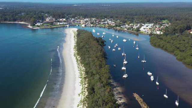 Aerial drone pullback reveal shot of Huskisson on the New South Wales South Coast, Australia, showing Currambene Creek and Jervis Bay on a bright sunny day   