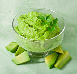 Avocado mousse with pieces of avocado fruit on a green textile background.