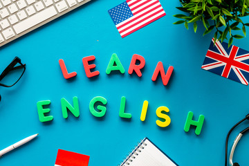 Learn English online. Concept with text, headset and keyboard on blue background top-down