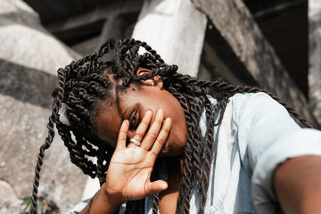 Happy young beautiful african american woman with pigtails and a piercing on her face covers her face with her hand, beautiful smilling happiness and joy - obrazy, fototapety, plakaty