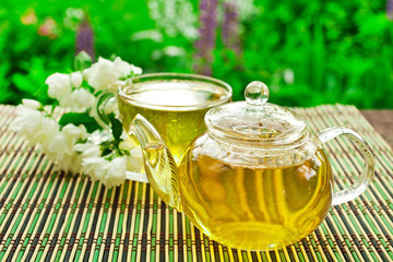 Jasmine green tea in a glass teapot with a glass cup and fresh blossoms.