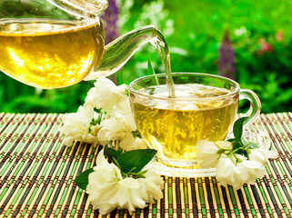 Jasmine green tea in a glass teapot with a glass cup and fresh blossoms.